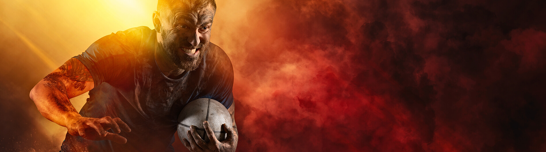 Very muddy man leaning forward with rugby ball in one arm