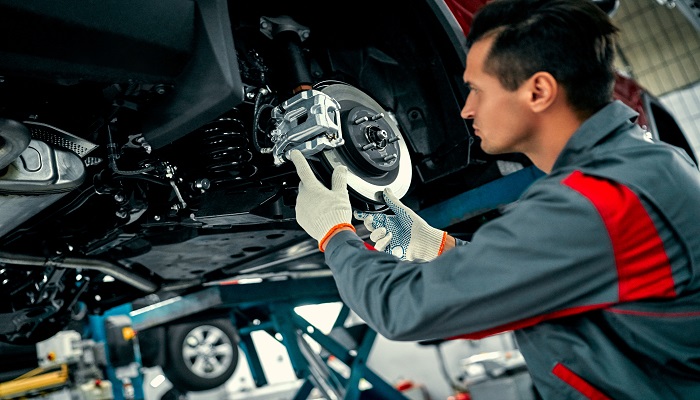 Young man repairing suspension of lifted automobile at auto repair garage shop station