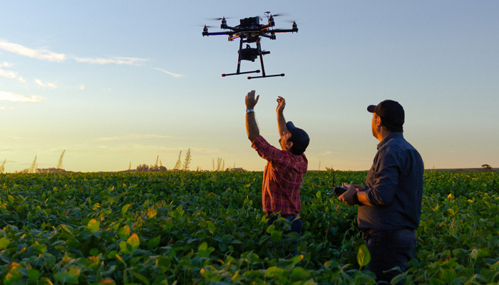 A man in a field reaching up at a drone carrying a camera